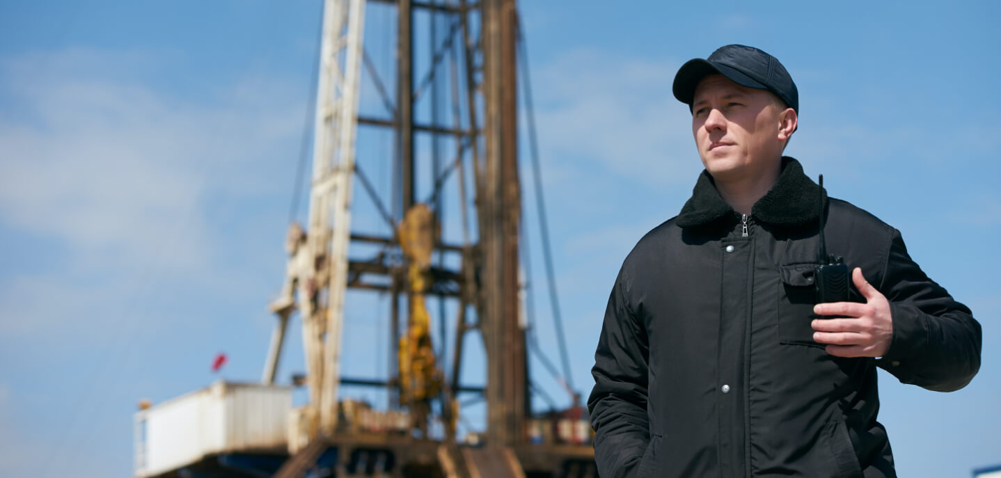 A security guard at an oil derrick site on patrol with his walkie talkie.