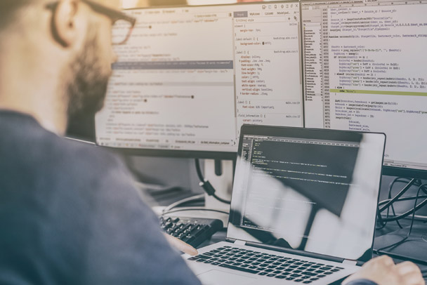 financial-forensic-due-diligence Man on a laptop computer and monitors with code on it.
