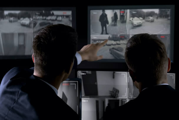 Two security personnel reviewing video security camera screens.