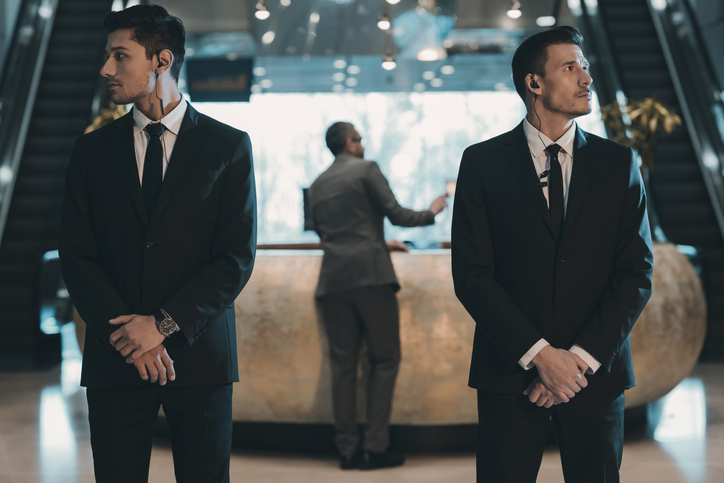 two bodyguards waiting for businessman standing at reception counter Two security operatives watching over front desk.
